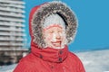 Funny cute adorable Caucasian smiling girl in red jacket parka squinting eyes from bright sun. Happy kid with snow on face at cold