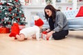 Adorable smiling infant crawling on the parquet to the christmas gifts near his mom which sits on the floor. Royalty Free Stock Photo