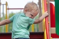 Funny cute caucasian blonde baby boy plays on the playground, climbing to upstair.