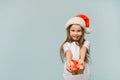 Funny cute girl in a santa hat gives a gift on a blue background with copy space. Concept of christmas and new year. Royalty Free Stock Photo