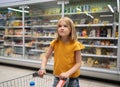 funny cute girl in supermarket with shopping cart wondered what to buy