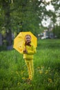 Funny cute girl wearing yellow coat holding colorful umbrella playing in the garden by rain and sun weather on a warm autumn or Royalty Free Stock Photo