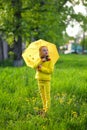 Funny cute girl wearing yellow coat holding colorful umbrella playing in the garden by rain and sun weather on a warm autumn or Royalty Free Stock Photo