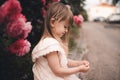 Funny cute kid girl 3-4 year old wear stylish dress posing with blooming pink flower roses in park at city street outdoors close u Royalty Free Stock Photo