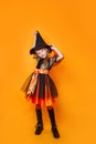 Funny little girl in witch Halloween costume on orange background Royalty Free Stock Photo