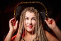 A funny cute plump woman with long pigtails in cowboy hat posing in dark studio. Girl on black background with alarming red light Royalty Free Stock Photo