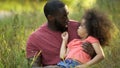 Funny dad and daughter making silly faces together, sitting in green grass