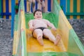 Funny delightful fat little caucasian boy in swimming trunks roll down on water slide during summer leisure vacation in amusement Royalty Free Stock Photo