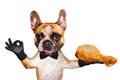 Funny dog ginger french bulldog waiter in a black bow tie hold a grilled chicken leg and show a sign approx. Animal isolated on Royalty Free Stock Photo