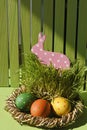 Funny Easter pink toy rabbit in a basket with colorful painted eggs Vertical