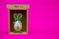 Funny egg in the form of cute bunny with wooden calendar set on april on pink background