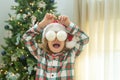 Funny excited child with Christmas balls on eyas near Christmas tree at home. Child preparing for the Christmas and New Royalty Free Stock Photo