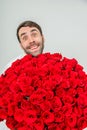 Funny expressive man isolated on white background, holding huge bunch of roses and looking from behind them with really Royalty Free Stock Photo