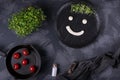 Funny face drawn with white sauce and microgreen on the black ceramic plate and cherry tomatoes on the cast iron pan Royalty Free Stock Photo