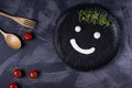 Funny face drawn with white sauce and microgreen on the black ceramic plate, cherry tomatoes and wooden cutlery Royalty Free Stock Photo