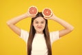 Funny face. Happy teenager girl hold grapefruit orangeisolated on yellow background, kids fruits vitamin.