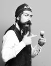 Funny face holding glass of alcoholic shot in vintage suede leather waistcoat with hat and glasses on blue studio Royalty Free Stock Photo