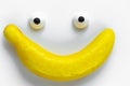 Funny face made of two toy eyes and an artificial banana instead of a mouth on a white background