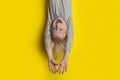 Funny fair-haired boy hanging upside down with arms outstretched and closed eyes. Portrait of child on bright yellow background