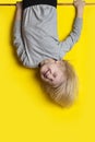Funny fair-haired boy hanging upside down on yellow background and grimace. Vertical frame