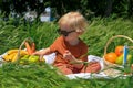 funny fair-haired boy with sunglasses holds an apple, basket with fruits on green grass Royalty Free Stock Photo