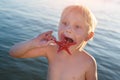 Funny fair-haired boy tries to eat starfish. Baby starfish on sea background
