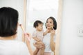 Funny family at home. Mother and her child girl are doing your makeup and having fun near mirror. Baby girl explores mother`s Royalty Free Stock Photo