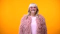 Funny fashionable aged lady in pink coat and round sunglasses smiling on camera