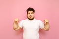 Funny fat guy with curly hair and beard shows piles down on copy space and looks into camera with surprised face, wearing white t- Royalty Free Stock Photo