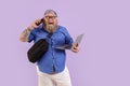 Funny fat male person with laptop and crossbody bag talks on phone on purple background