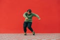 Funny fat man in casual clothes shows hip hop performance on the street against the backdrop of a red wall with a smile on his Royalty Free Stock Photo