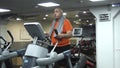 Funny fat man doing exercises on the ellipsoid in gym