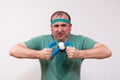 A funny fat man in a green bandana and t-shirt clutches an expander with a grimace of physical effort. home fitness