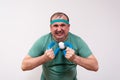 A funny fat man in a green bandana and t-shirt clutches an expander with a grimace of physical effort. home fitness