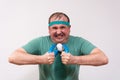 A funny fat man in a green bandana and t-shirt clutches an expander with a grimace of physical effort. home fitness training,