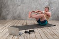 Funny fat man in sports clothes doing exercises. He plays sports remotely while looking at his laptop Royalty Free Stock Photo