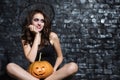 Funny female witch posing with pumpkin in studio.