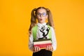 Funny First-Grade Schoolgirl Holding Stack Of Books And Microscope