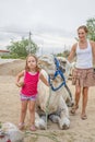Funny little girl making faces with dromedary sitting in countryside on summer and mother