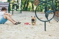 Funny french puppy bulldog and teenager playing games outside. Adorable orange bulldog in blue harness in the playground on sand. Royalty Free Stock Photo