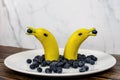 Funny fruit figure two banana dolphins with blueberries on a white plate Royalty Free Stock Photo