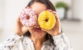 Funny gesture of a woman looking through holes of two different types of donuts