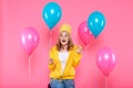 Girl in birthday hat, balloons and blowout horn on pastel pink background. Attractive trendy teenager celebrating birthday.