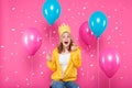 Funny girl in birthday hat, balloons and flying confetti on pastel pink background. Attractive teenager celebrating birthday. Royalty Free Stock Photo