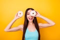 Funny girl in blue singlet with beaming smile holding white tasty donuts near eyes, fooling around on bright yellow background. Pr Royalty Free Stock Photo