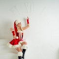 Funny girl in Christmas outfit points to watch. Red Santa suit with hood. Royalty Free Stock Photo