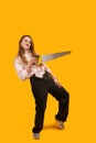 Funny girl dancing with hand saw in her hands. Modern young woman posing with saw in studio on yellow background. Vertical frame. Royalty Free Stock Photo