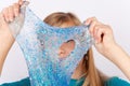 Funny girl holding a transpareng blue glitter slime with a hole in front of her face Royalty Free Stock Photo