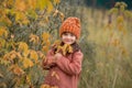 Funny girl in an orange hat and a brown coat holds a branch with yellow leaves and smiles. horizontal photo of a child in the fall
