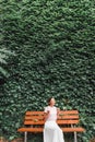 Girl posing on a bench in Park against a huge wall with ivy